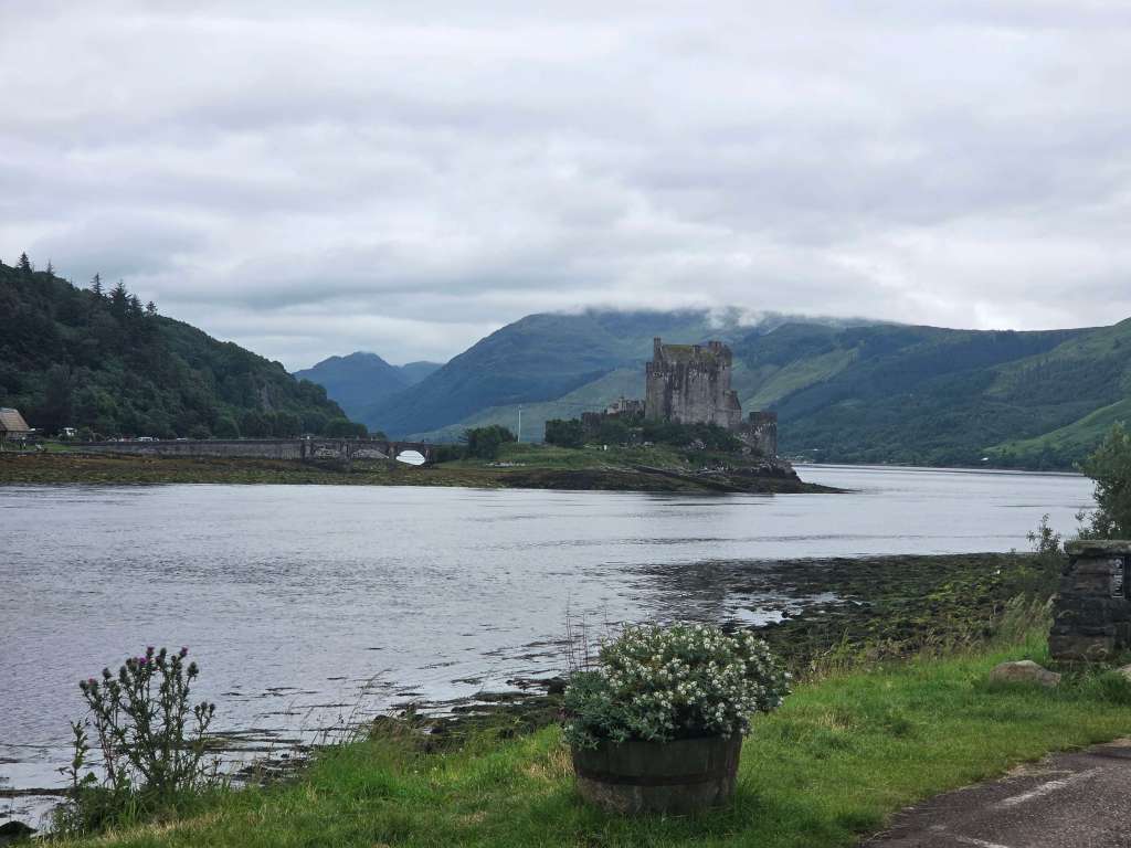 A scenic picture of a castle in the middle of a lake in Scotland, surrounded by hills on a cloudy day.
